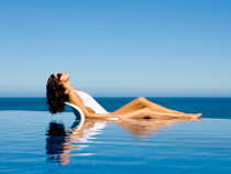 Frau im weißen Badeanzug vor einem Infinity Pool.